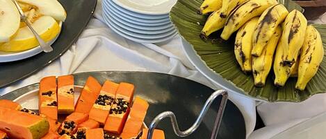 Uma mesa de buffet com diversos alimentos, incluindo melancia, bananas e mamão.