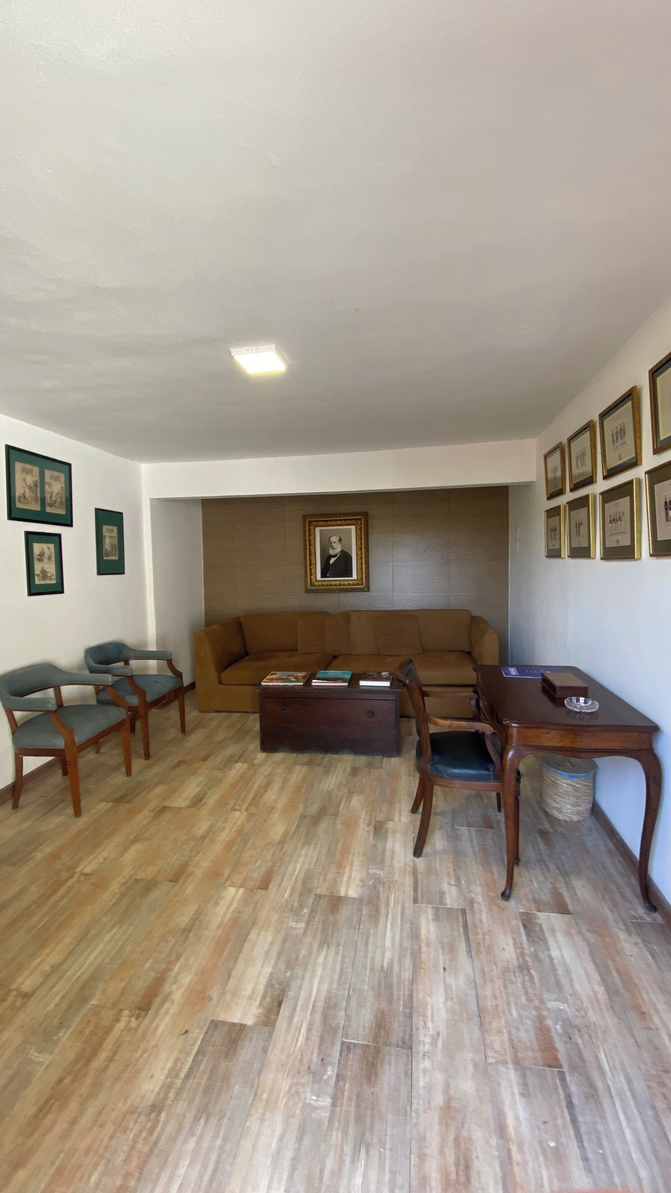 A living room with a brown sofa, wooden chairs, a coffee table, and a wall-mounted picture frame.