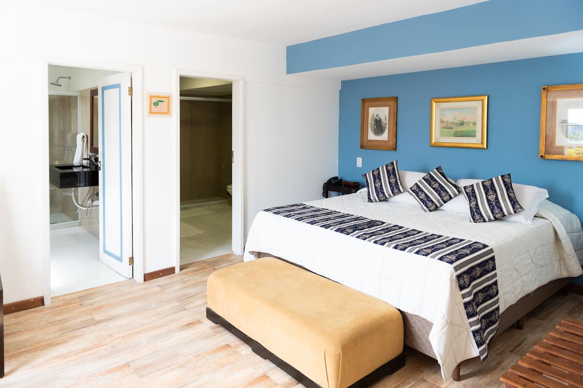 Un dormitorio con cama, un banco, baño y un pasillo.