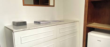 A white cabinet with drawers, a small refrigerator, and a wooden shelf unit.