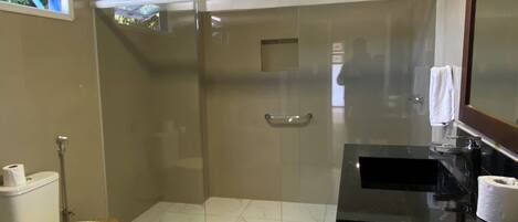 Un baño moderno con ducha de vidrio, inodoro y lavamanos con encimera negra.