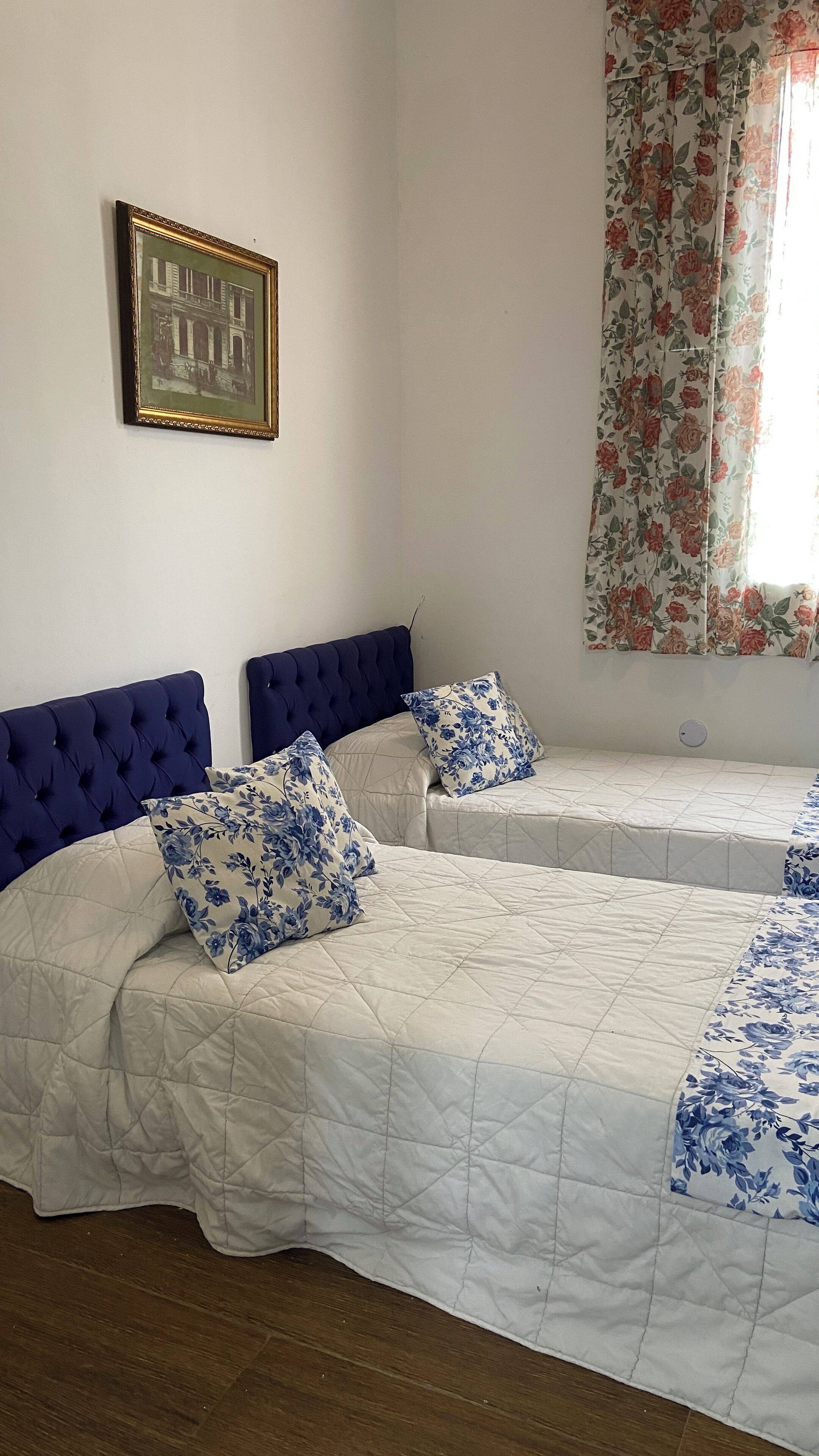 Una habitación con dos camas, cada una con cabecera azul y almohadas con estampado floral.