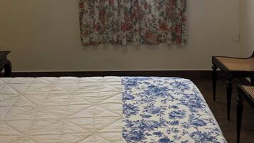 A bedroom with a bed, a chair, a window with floral curtains, and two framed pictures on the wall.