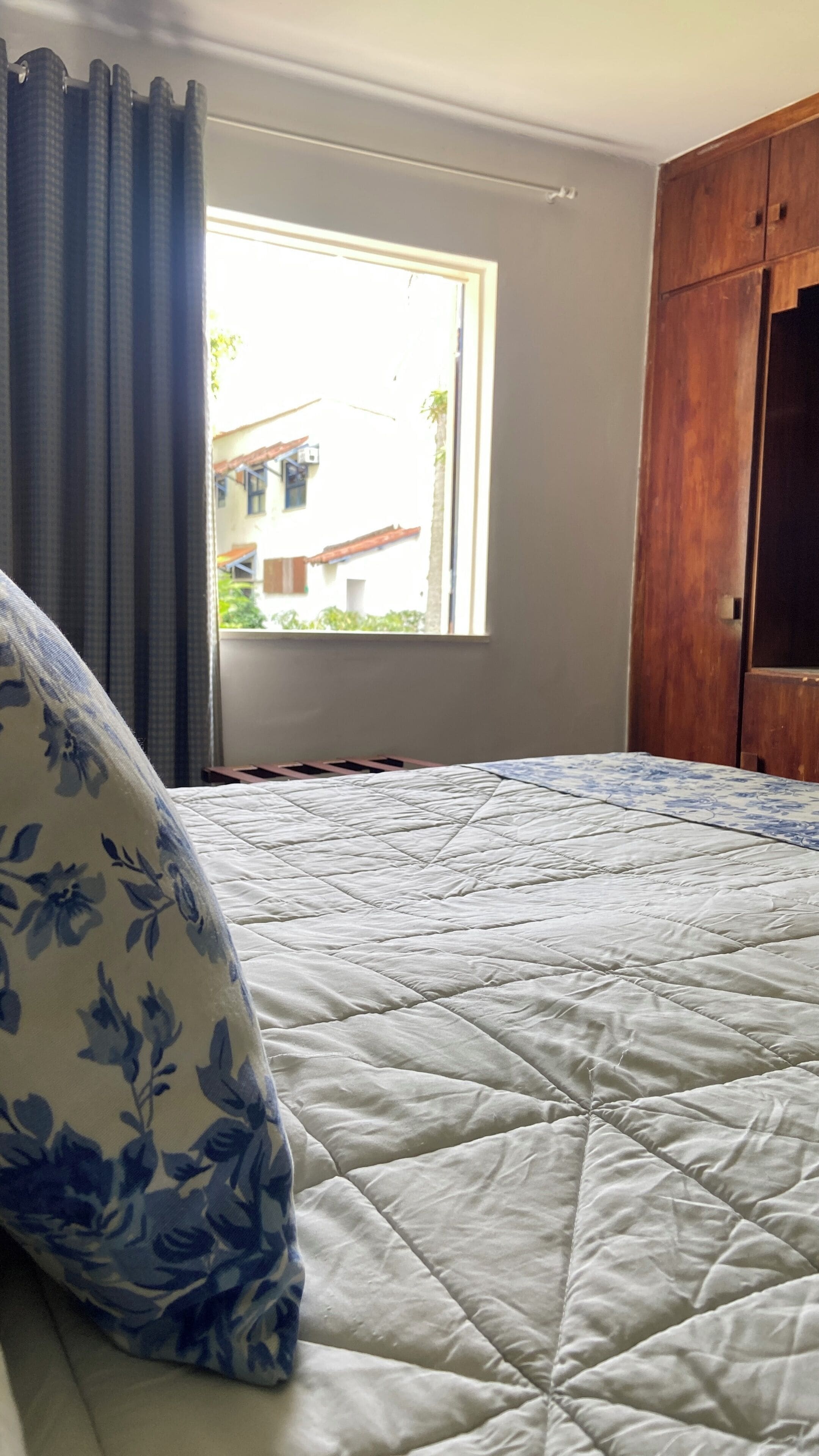 A bedroom with a bed, a window, and a wooden wardrobe.