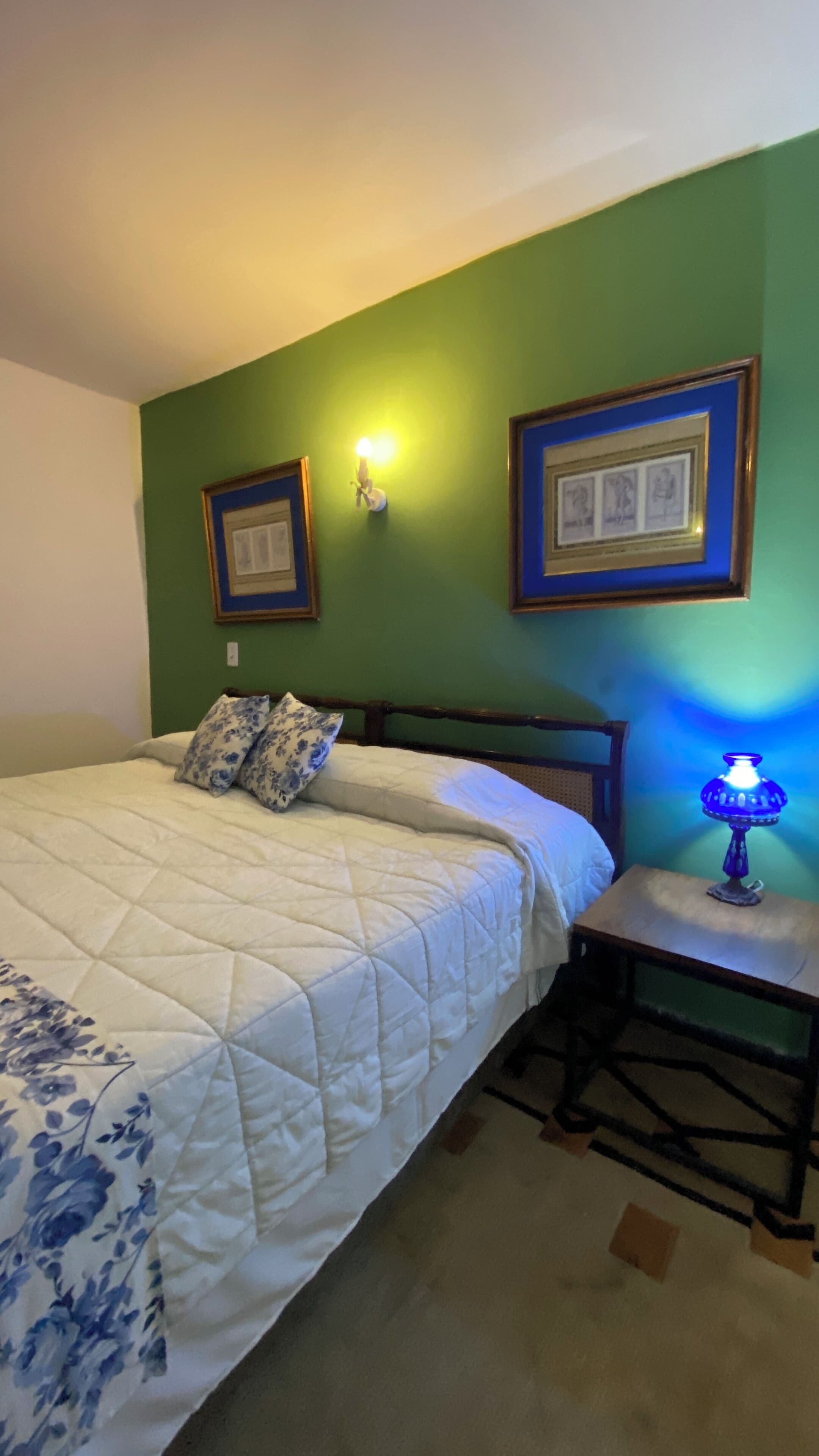 A bedroom with a bed, a nightstand, a lamp, and two framed pictures on the wall.
