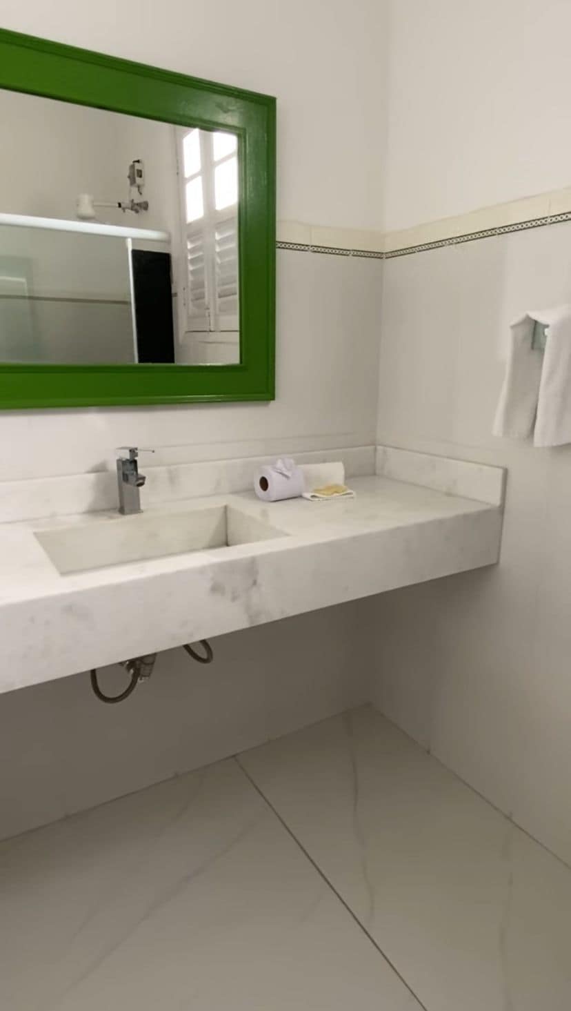 Ein Badezimmer mit einem weißen Waschbecken, einem spiegel mit grünem Rahmen und einem Handtuch an der Wand.