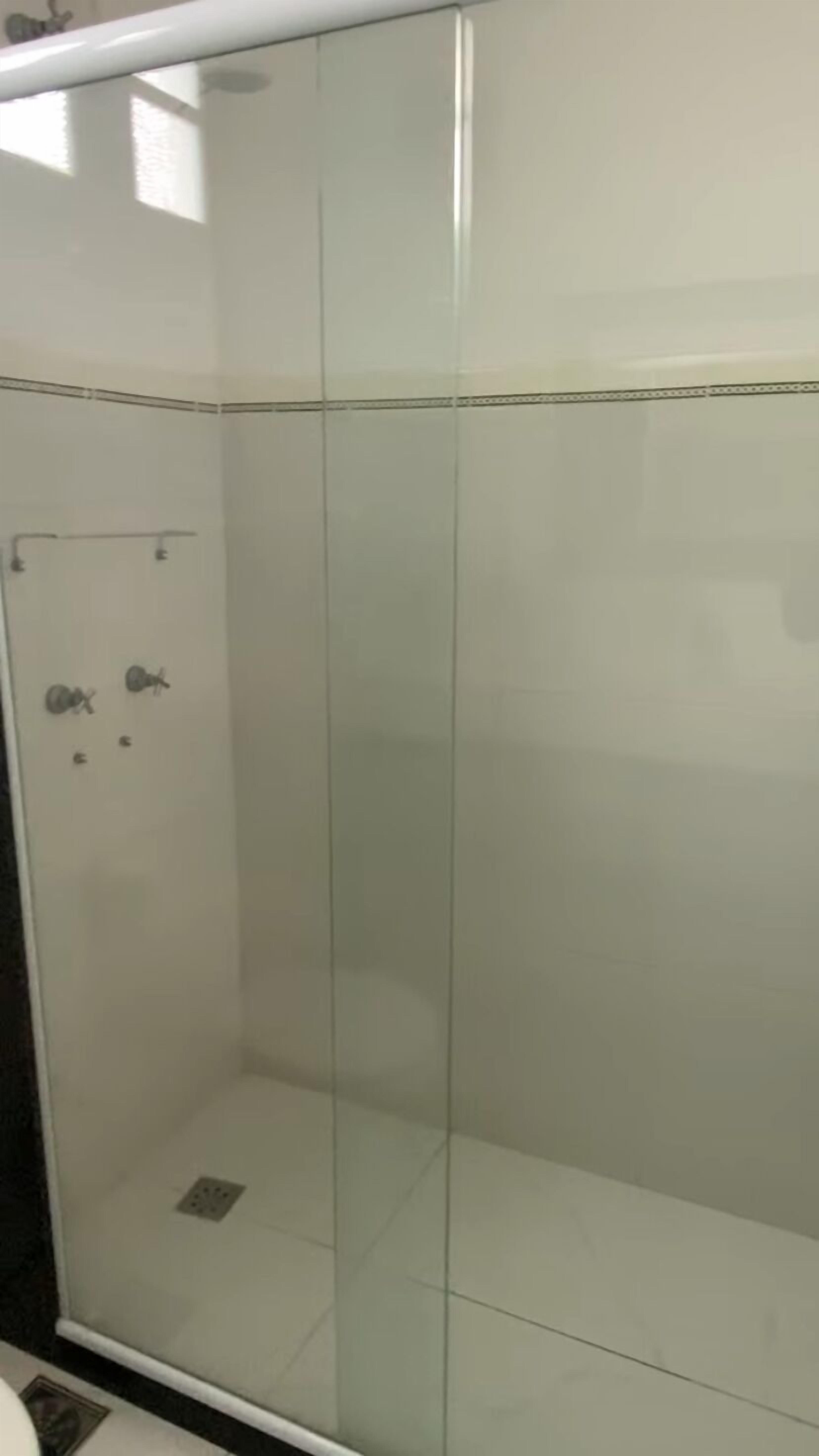 A bathroom with a glass shower enclosure, a white tiled wall, and a visible drain.