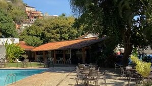 Uma área à beira da piscina com piso de pedra, mobiliário de exterior e um edifício com telhado vermelho.