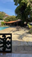 Uma área à beira da piscina com piso de pedra, mobiliário de exterior e um edifício com telhado vermelho.
