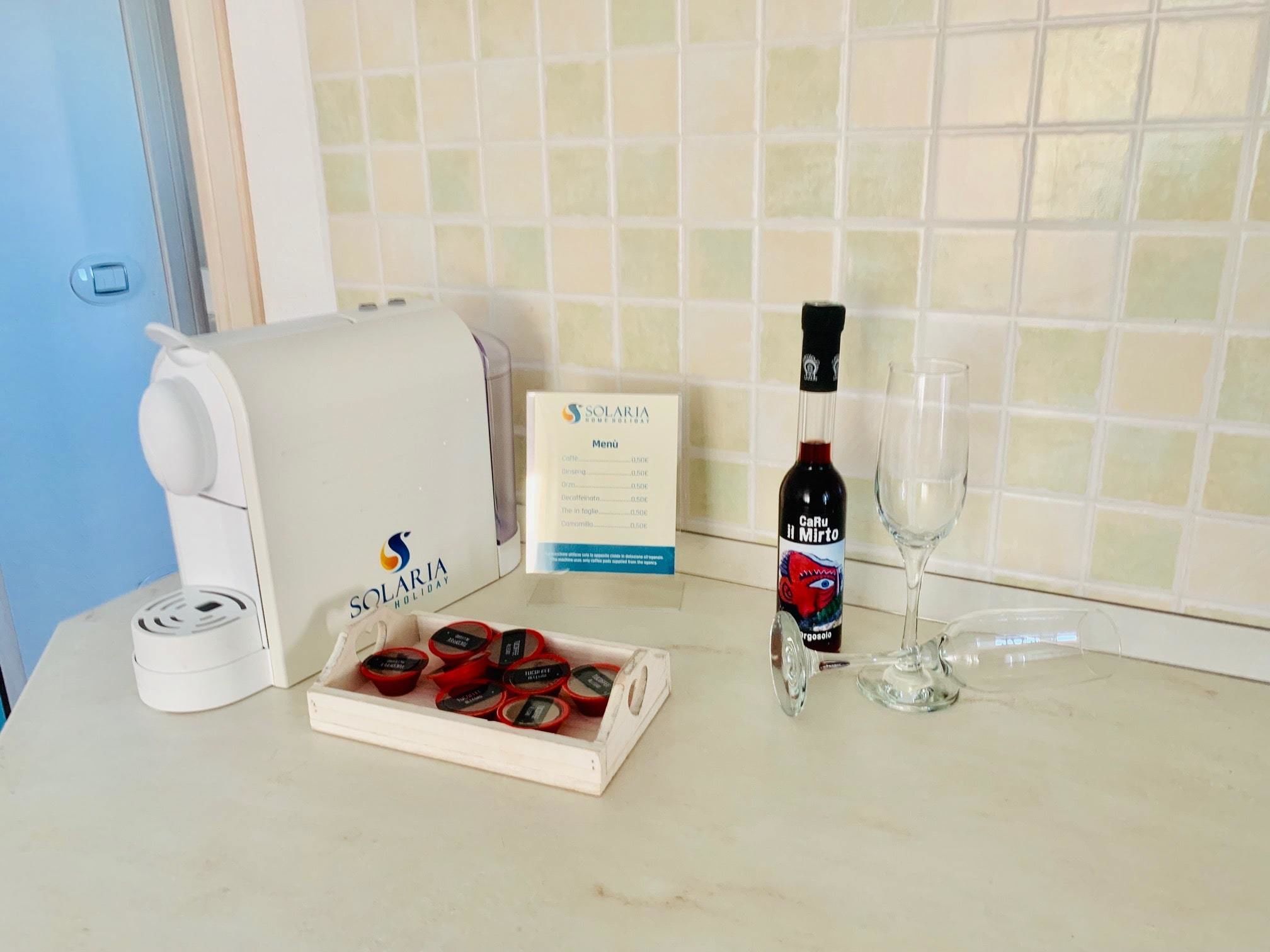 Una encimera de cocina con una cafetera, un menú, una botella de vino y una copa.