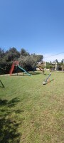 Un parque infantil con tobogán y estructura para escalar, rodeado de árboles y cielo despejado.