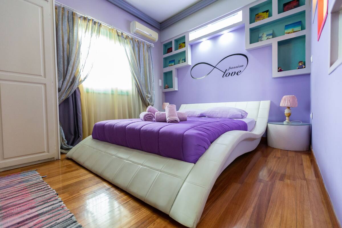 A bedroom with a bed, a nightstand, a wall shelf, and a window with curtains.
