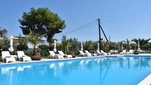 Una piscina con sillas de descanso y sombrillas, rodeada de árboles y edificios.
