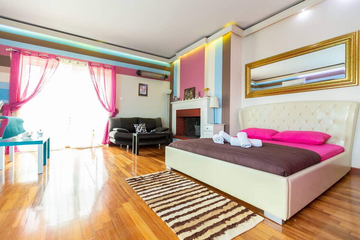 A bedroom with a bed, a sofa, a table, and a fireplace.