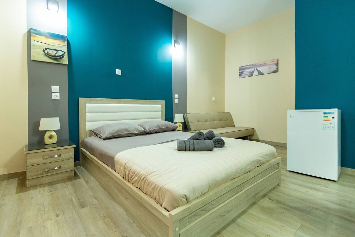 A bedroom with a bed, bedside table, lamp, and a refrigerator.