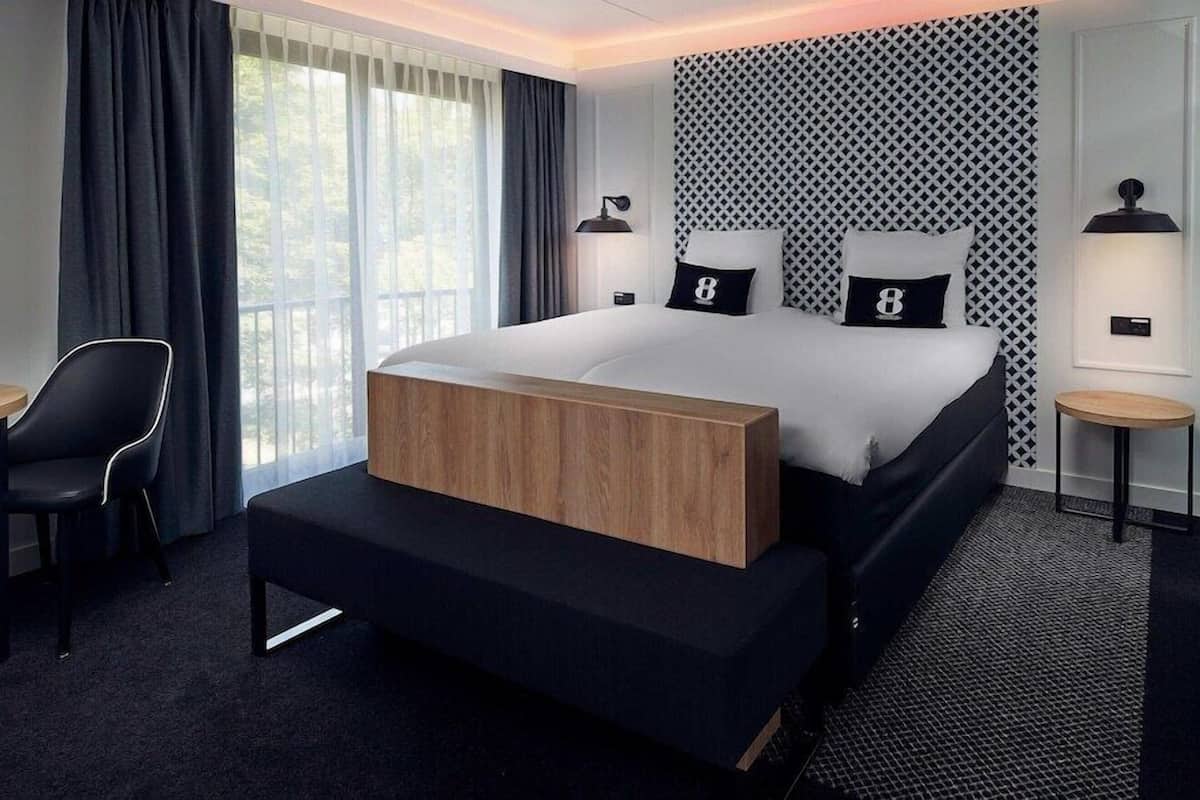 Een moderne hotelkamer met een groot bed, een houten nachtkastje, een bureau en een stoel.