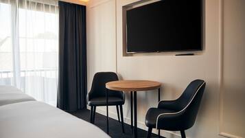 Habitación de hotel con cama, dos sillas, una mesita, televisor y ventana con cortinas.