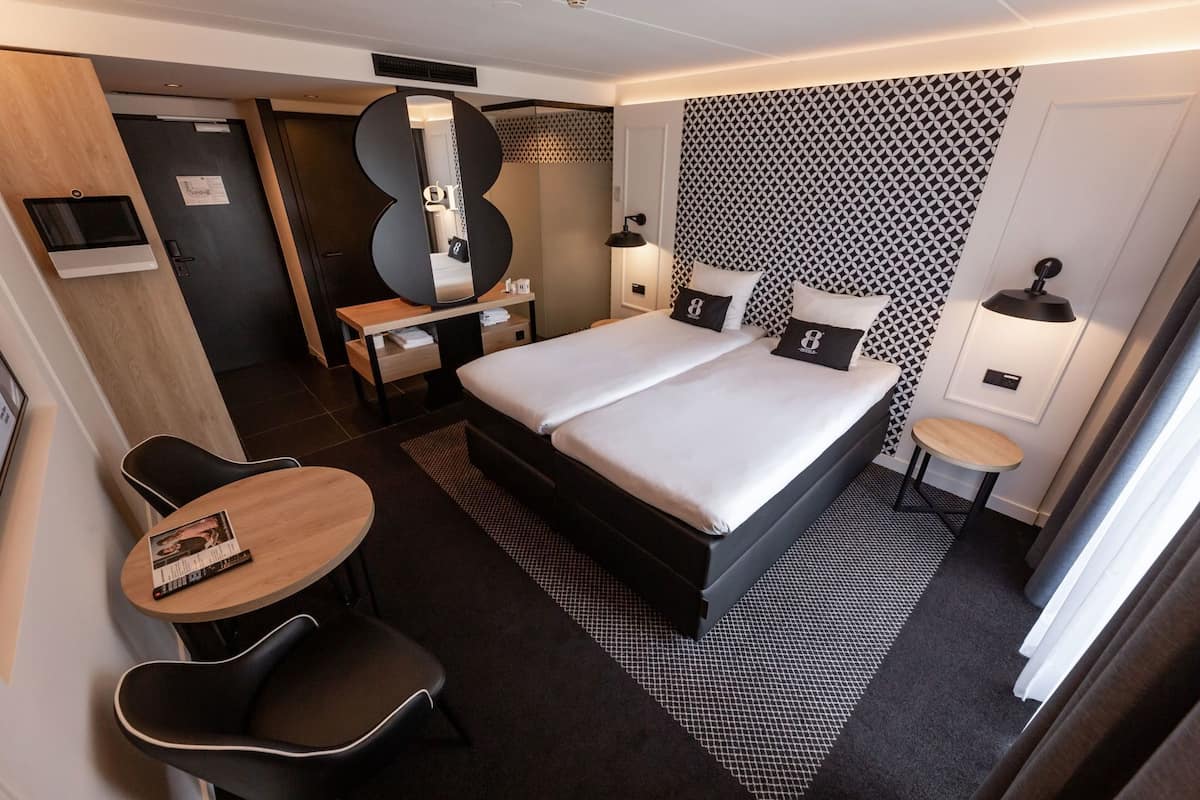 Een hotelkamer met een bed, bureau, stoel en een grote spiegel.