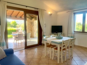 Une pièce comprenant une table à manger, des chaises, un canapé bleu, un téléviseur et une porte-fenêtre coulissante donnant sur un espace extérieur avec une table et des chaises.