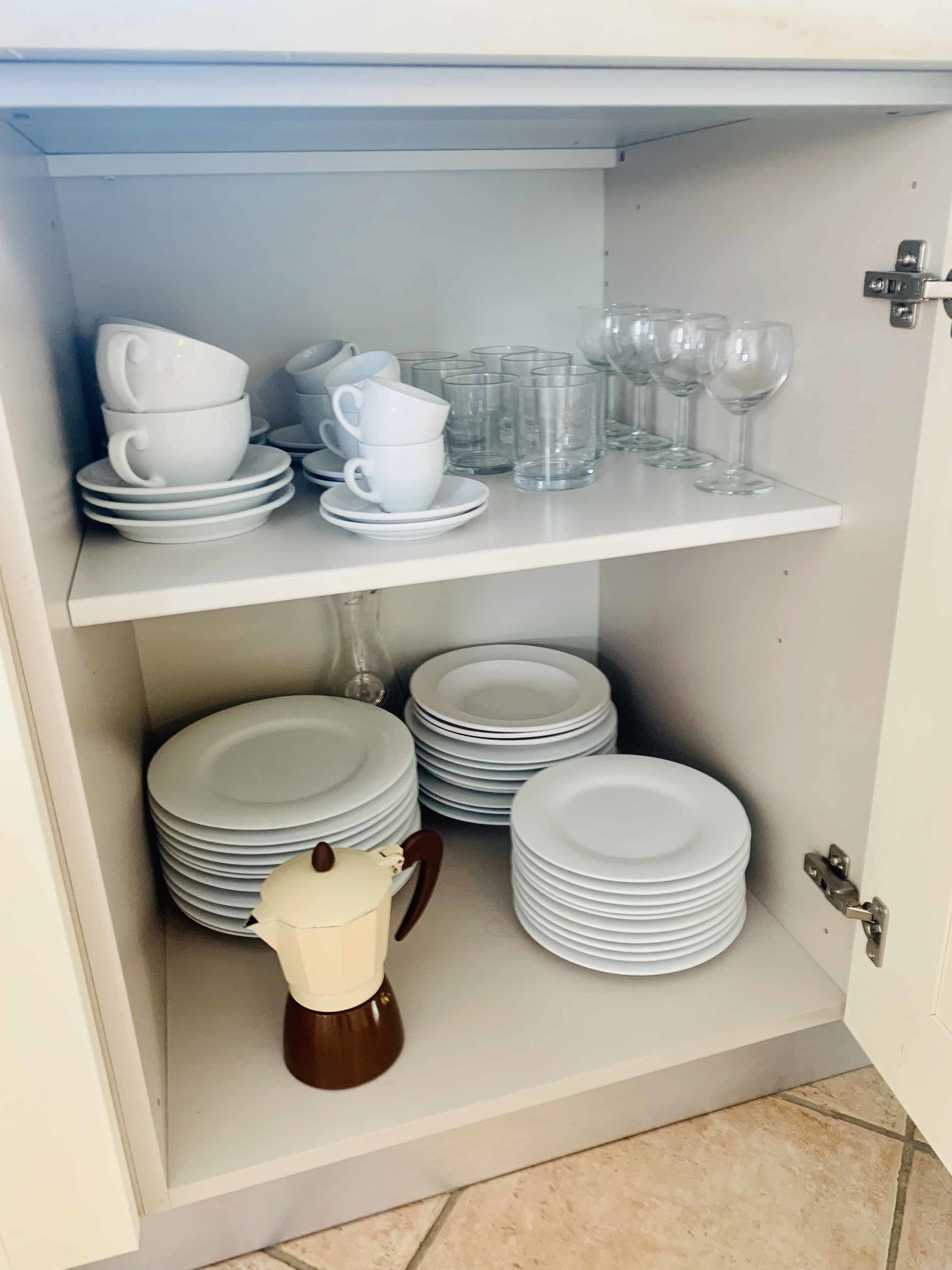 A storage cabinet with multiple shelves holding stacks of white plates, cups, and glasses.