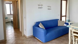 A room with a blue sofa, a dining table with chairs, a ceiling fan, and an air conditioning unit. - Solaria Apartment VIII (Budoni)