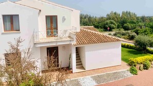 A two-story white building with a tiled roof, a balcony, and a garage. - Solaria Apartment VIII (Budoni)