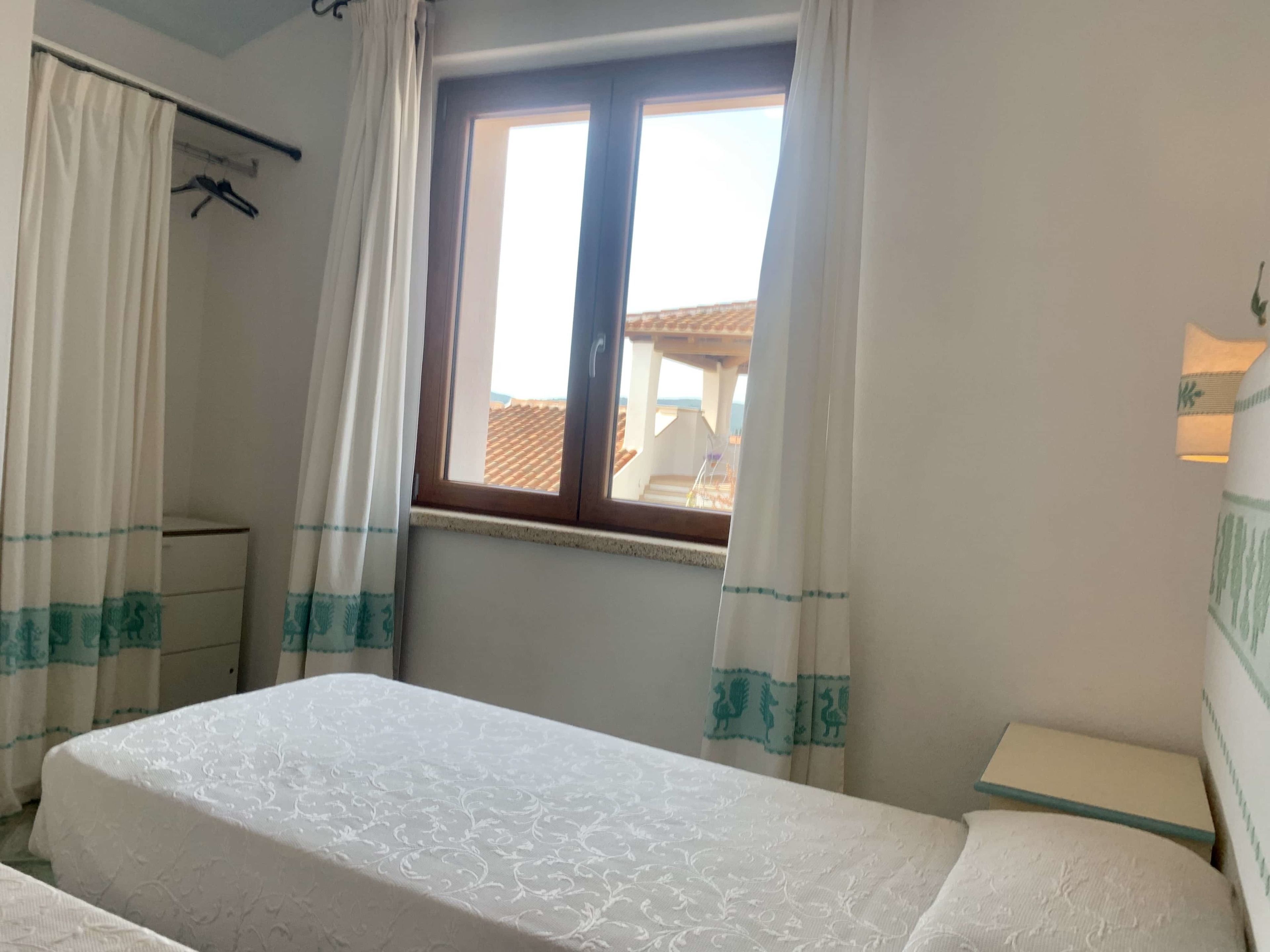 A bedroom with a bed, a window with curtains, a bedside table, and a wardrobe.