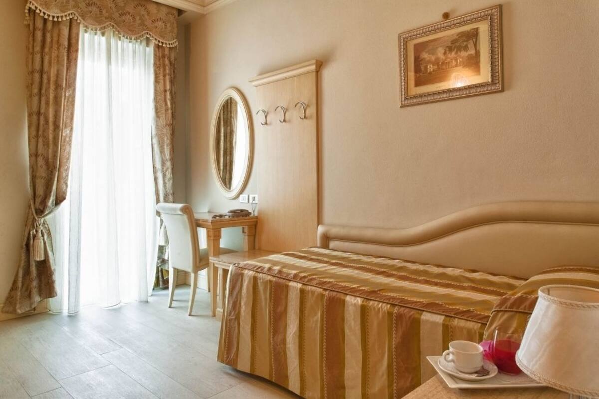 A hotel room with a bed, a desk, a chair, a mirror, and a framed picture on the wall.