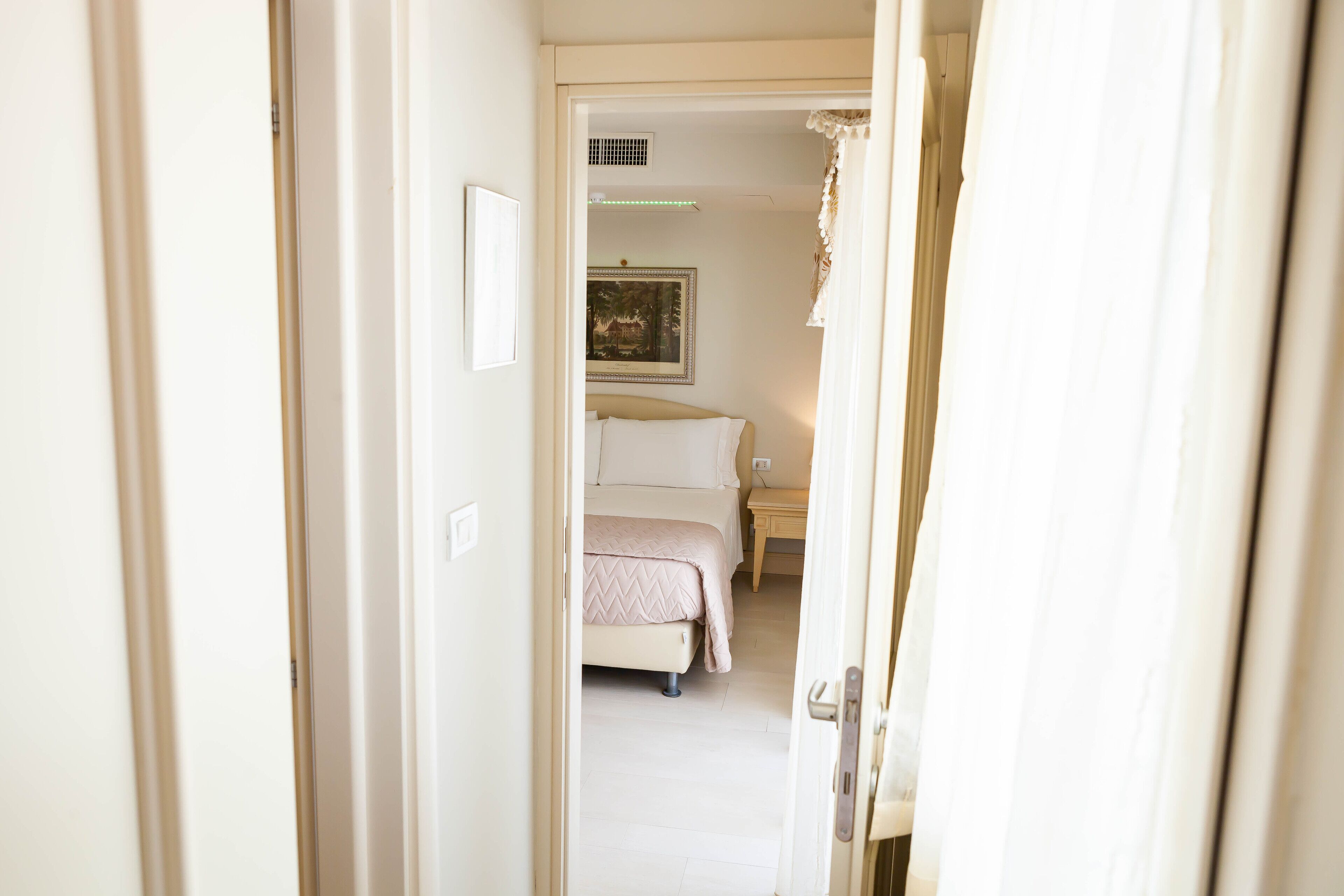 A narrow hallway leading to a bedroom with a bed, a nightstand, and a framed picture on the wall.