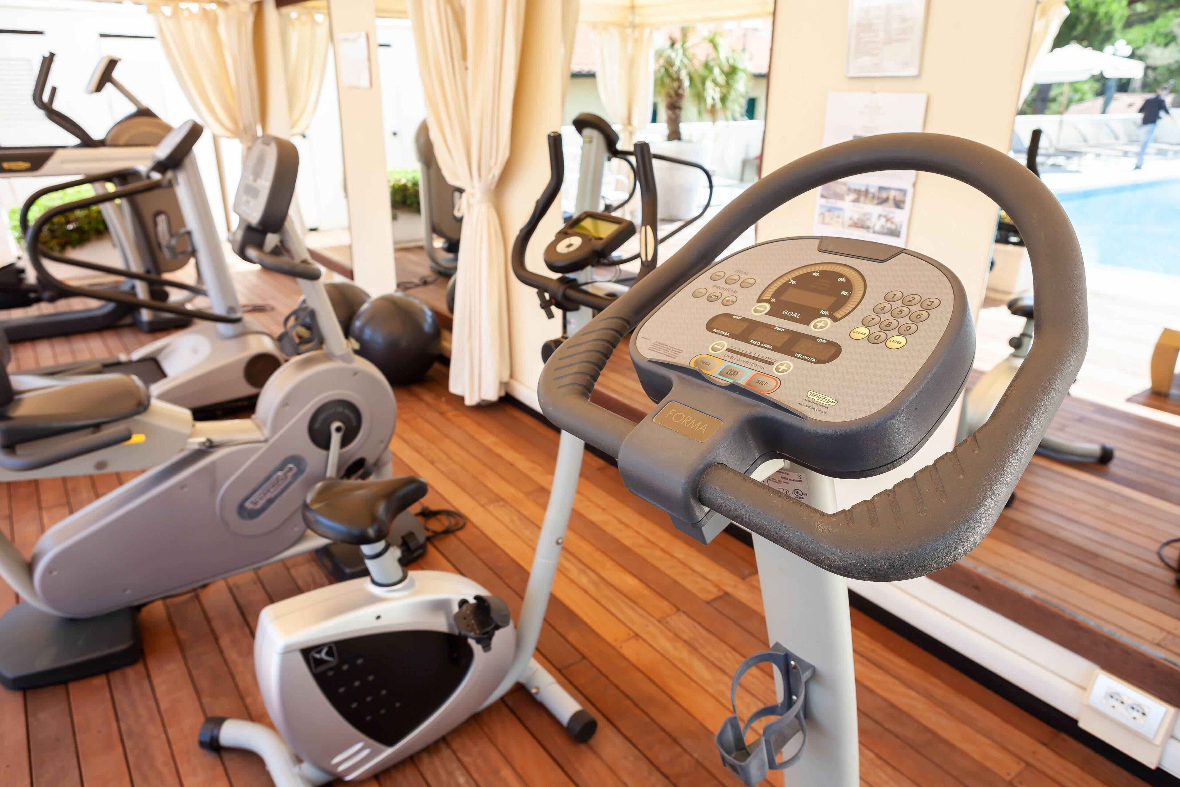 A stationary bike with a digital display and control panel, positioned on a wooden floor with other exercise equipment in the background.