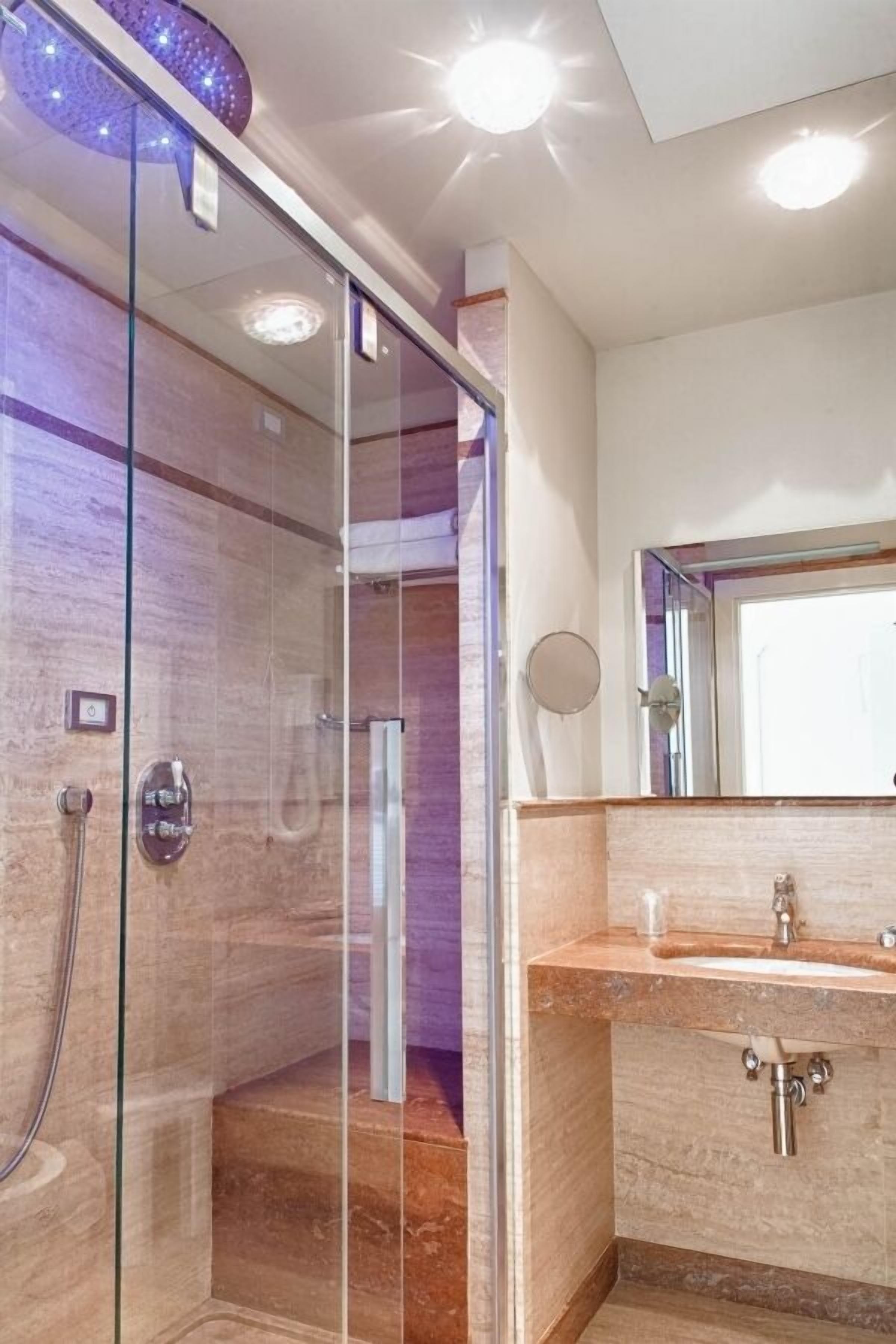 A modern bathroom with a glass shower enclosure, a marble-topped sink, and a large mirror.