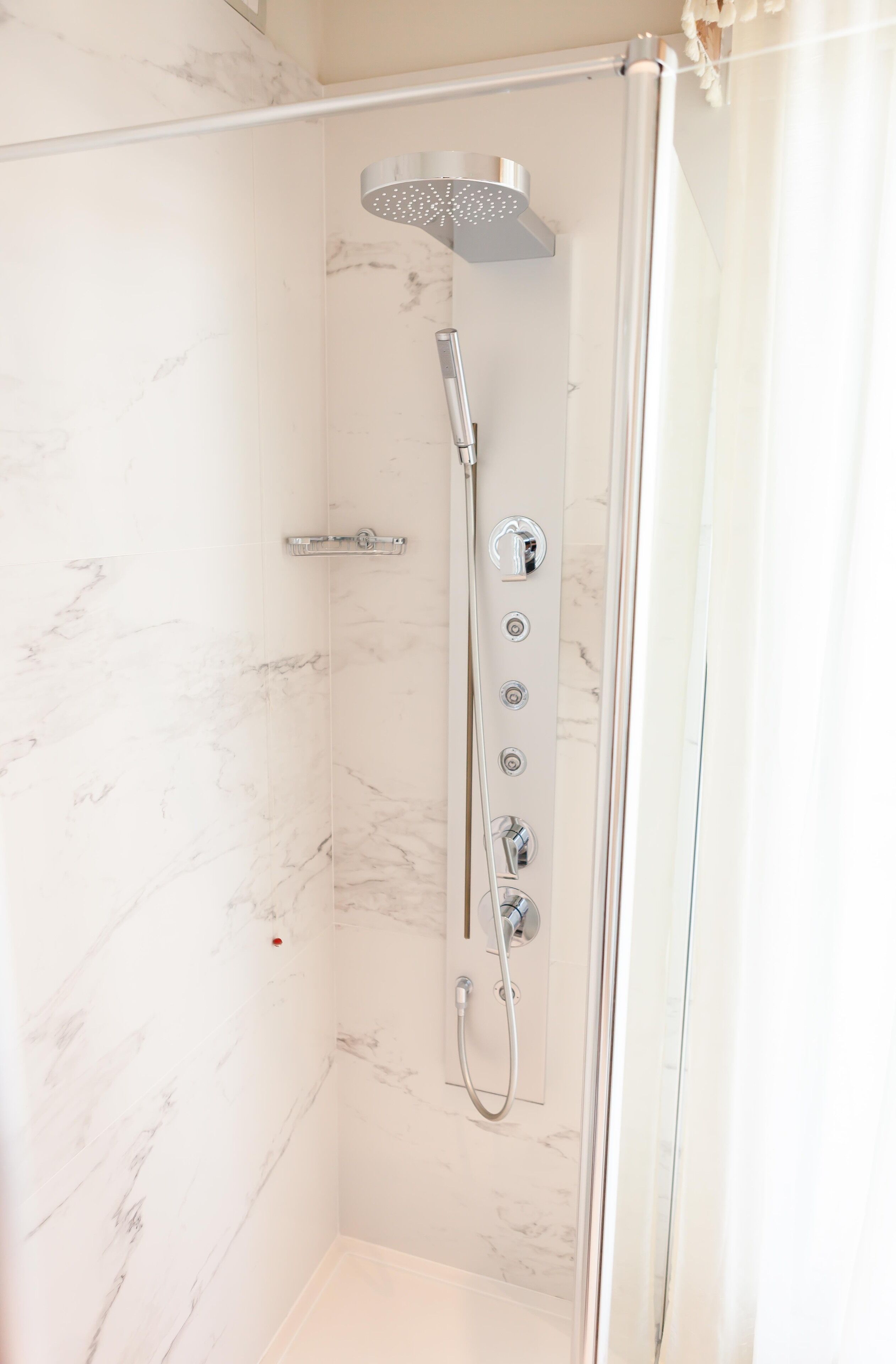 A glass-enclosed shower with a handheld showerhead and a wall-mounted control panel.