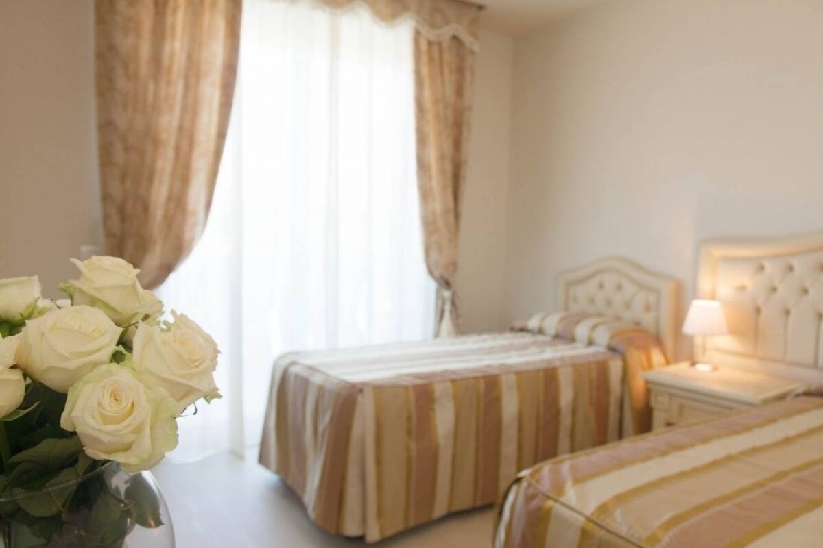 A hotel room with two beds, a nightstand with a lamp, and a vase of white roses on a table.