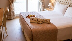 A neatly made bed with a quilted cover, a bedside table with a lamp, and a chair. - Hotel Conchiglia (Cervia)