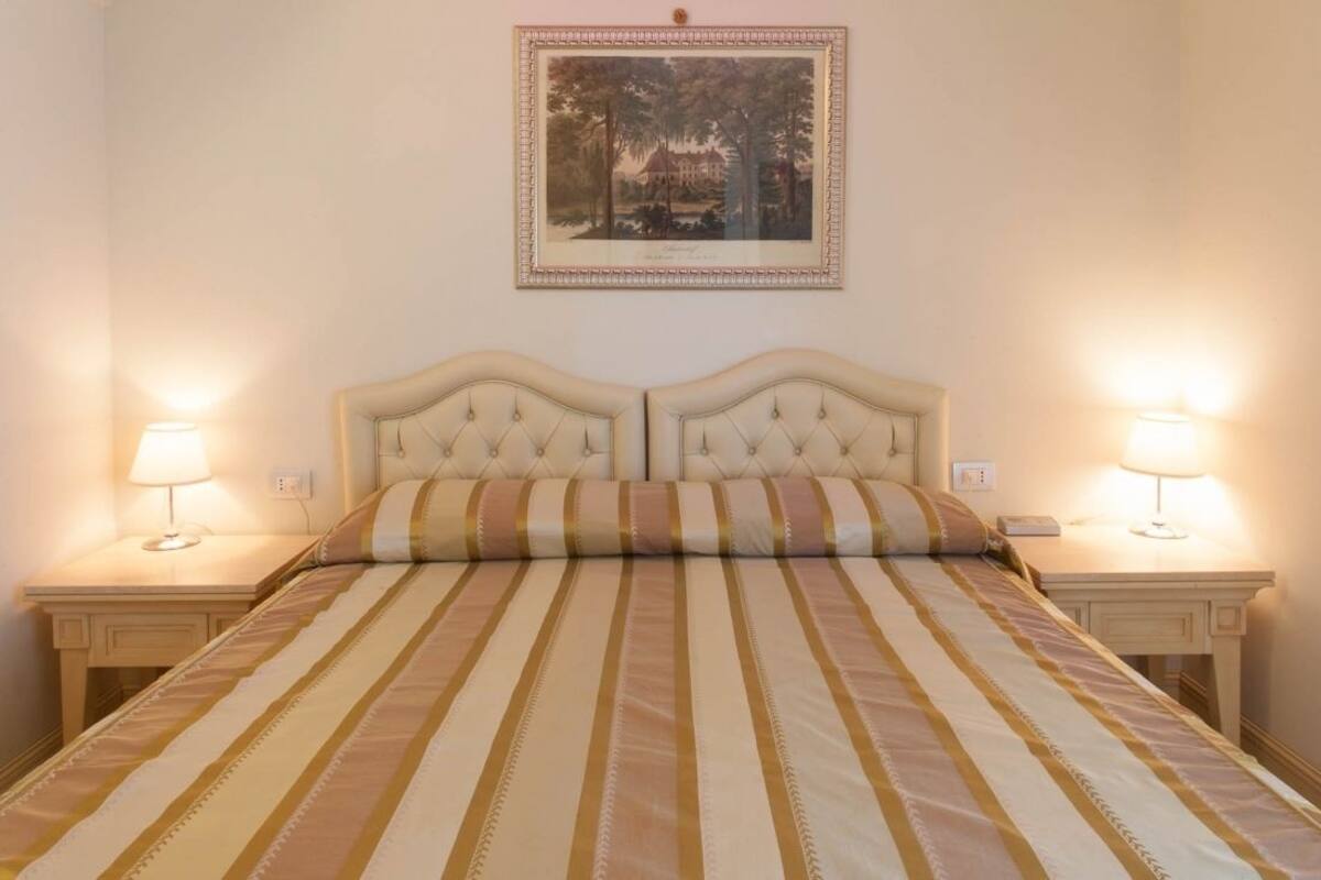 A double bed with striped bedding, two bedside tables with lamps, and a framed picture on the wall.