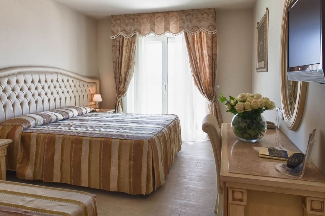 Une chambre d’hôtel avec un grand lit, un bureau agrémenté d’un vase de fleurs et un téléviseur fixé au mur.