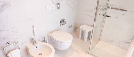 A modern bathroom with a marble floor, a white sink, a toilet, and a glass shower enclosure.