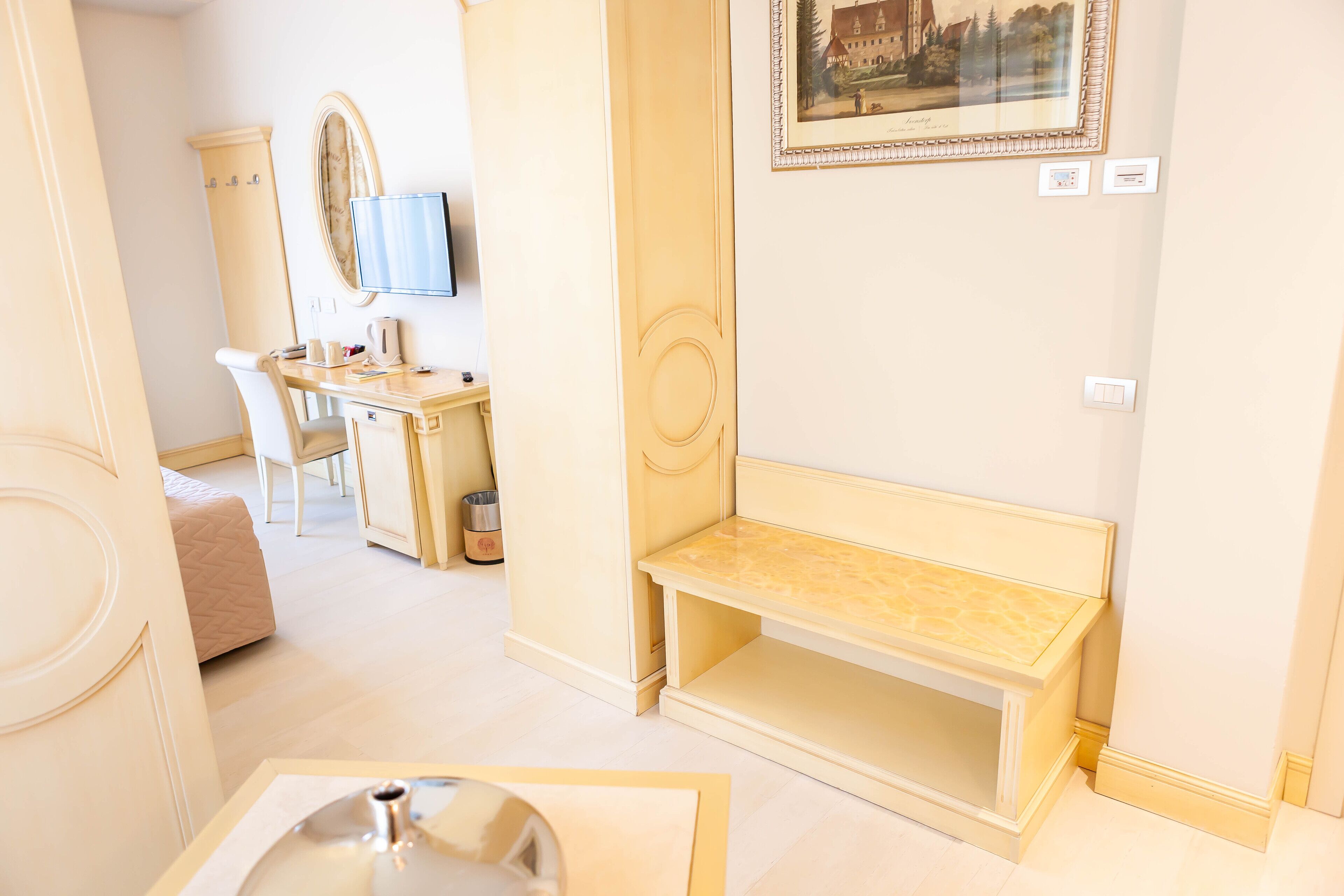 Habitación de hotel con cama, escritorio, silla, espejo, televisor y un cuadro en la pared.