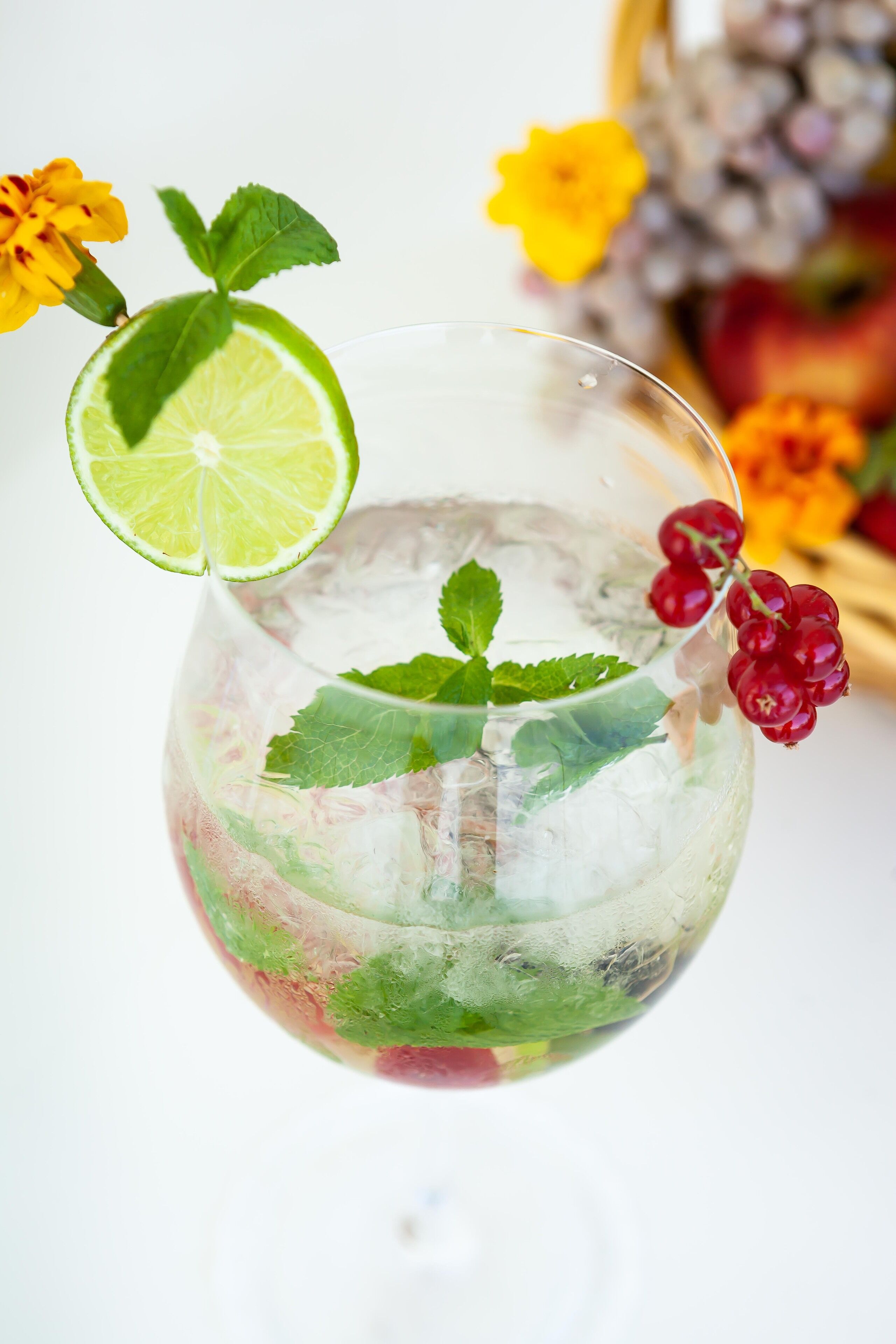Un vaso transparente con rodaja de lima y hojas de menta, rodeado de hielo y bayas.
