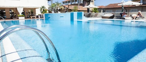 Una piscina con borde de agua cristalina, rodeada de sillas de descanso y sombrillas, con edificios al fondo.