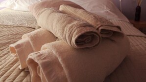A neatly made bed with rolled towels, a wall with a mosaic of stones and wood, and two wall-mounted lamps.