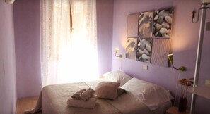 A bedroom with a bed, pillows, a bedside table, a lamp, and a wall-mounted artwork. - Affittacamere Mariuccia (Montalcino)