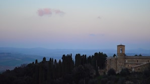 A historic building with a bell tower, surrounded by trees and overlooking a valley.