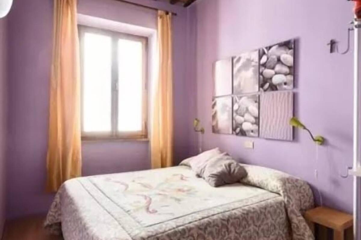 Un dormitorio con cama, ventana con cortinas y una obra de arte en la pared.