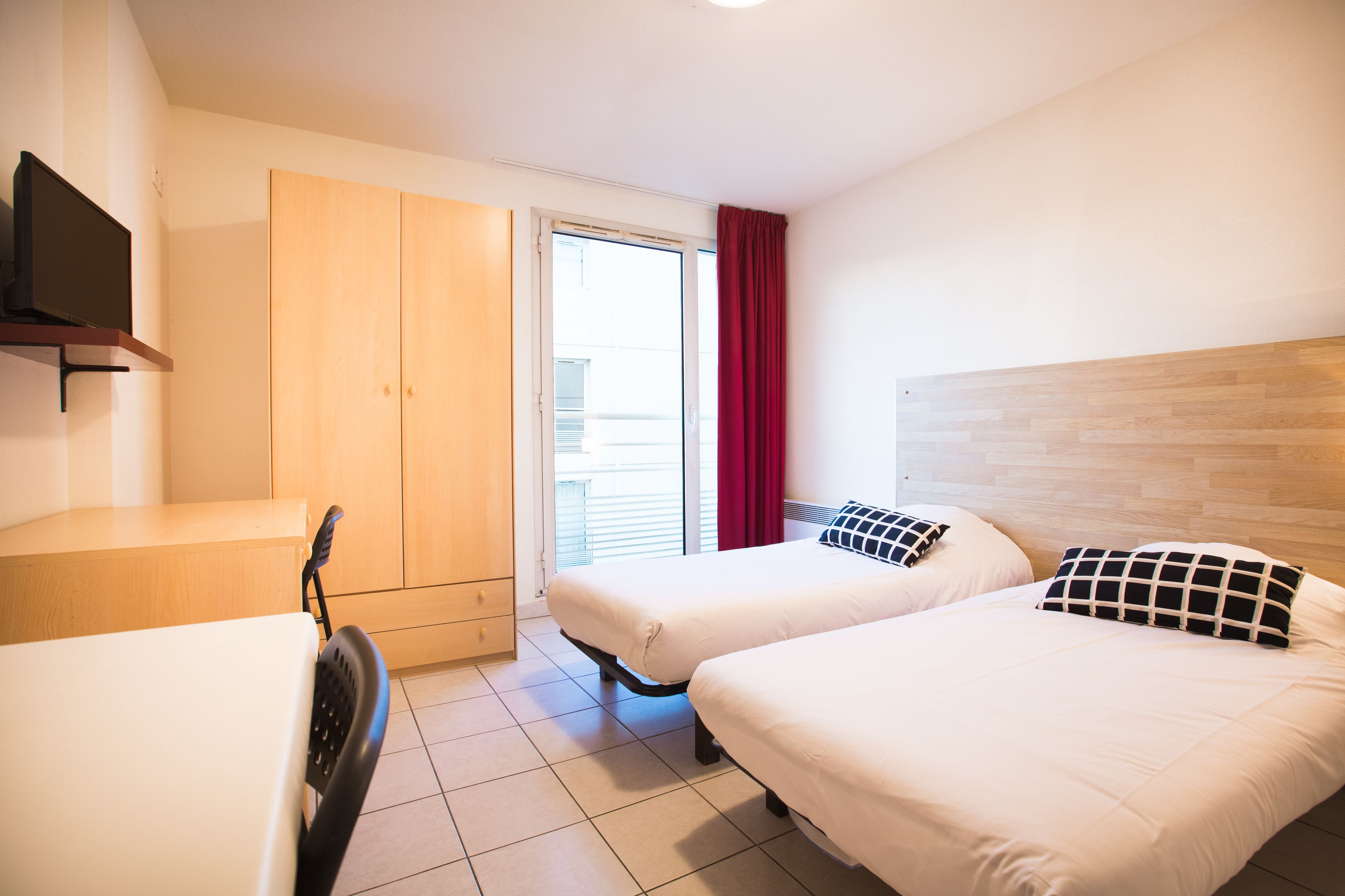 A hotel room with two beds, a TV, a wardrobe, and a desk.