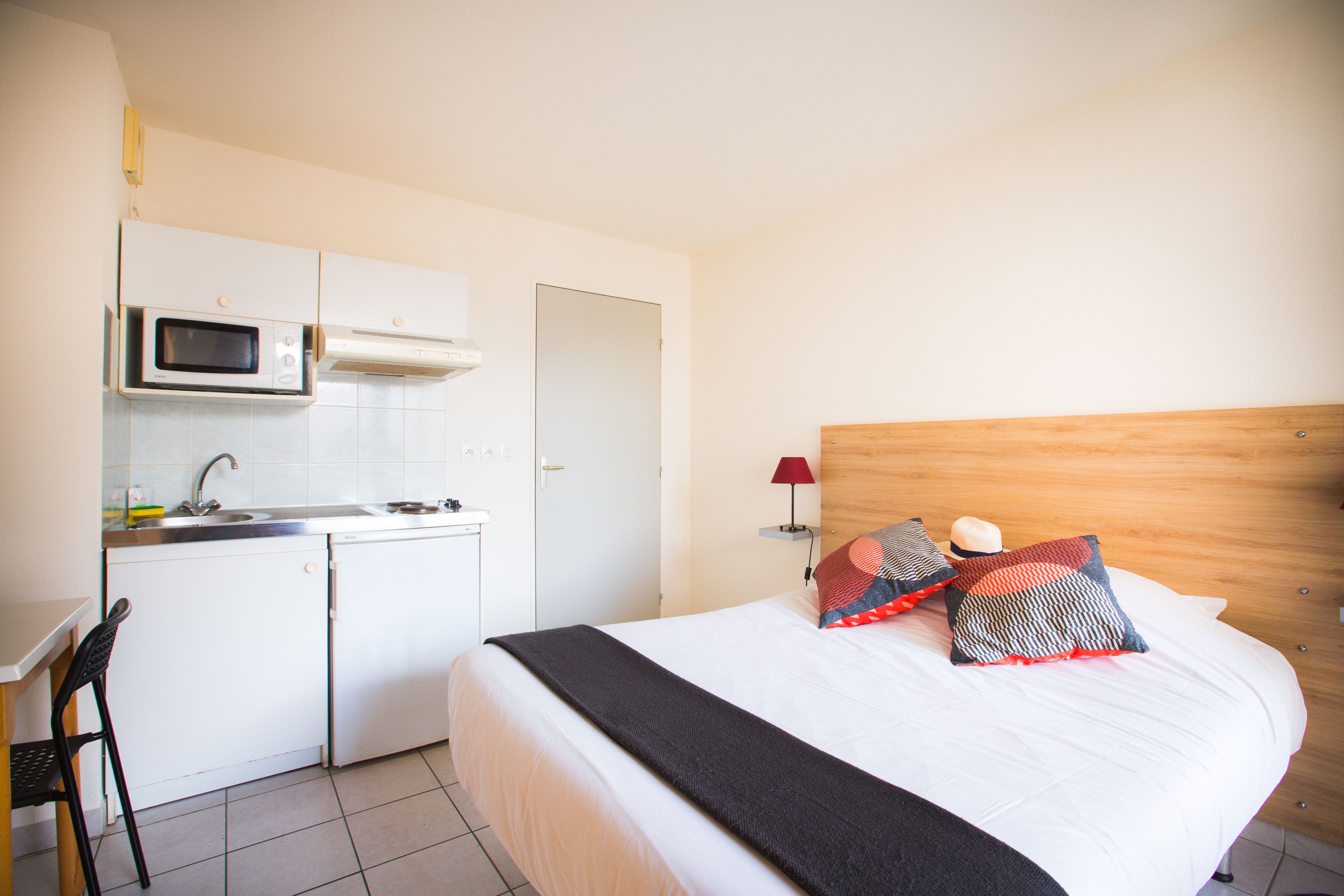 Habitación de hotel compacta con cama, kitchenette pequeña y una sola silla.