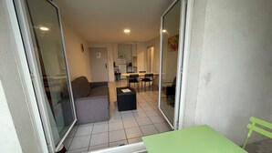 Un appartement moderne doté d’une porte-fenêtre coulissante donnant sur un balcon, d’une table verte et d’un coin cuisine à l’arrière-plan.