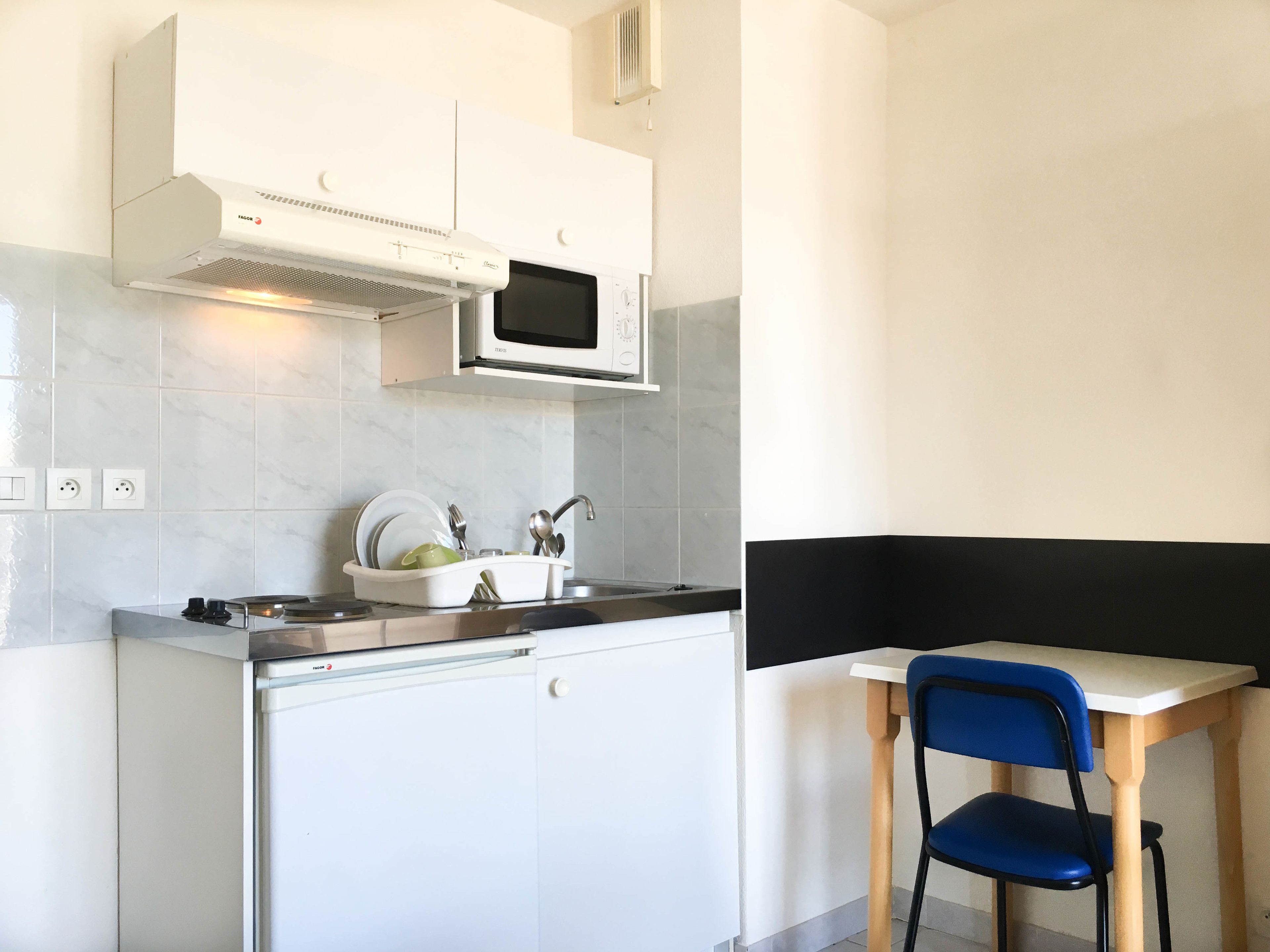 Une cuisine compacte équipée d’un four à micro-ondes, d’une cuisinière et d’un évier. Un petit coin repas avec une table et une chaise est également disponible.