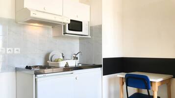 Une cuisine compacte équipée d’un four à micro-ondes, d’une cuisinière et d’un évier. Un petit coin repas avec une table et une chaise est également disponible.