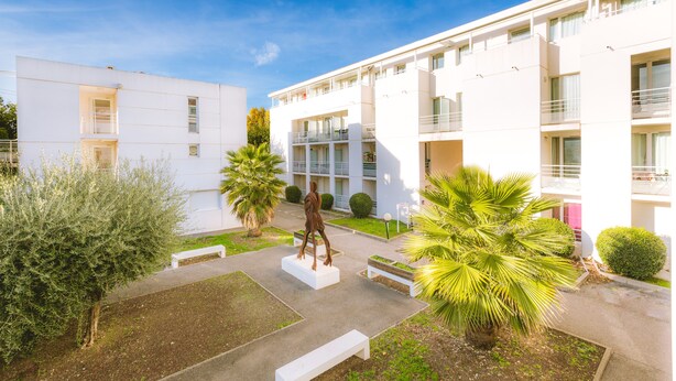 Un bâtiment moderne doté d’une cour intérieure, où l’on trouve une statue, des bancs et des palmiers.